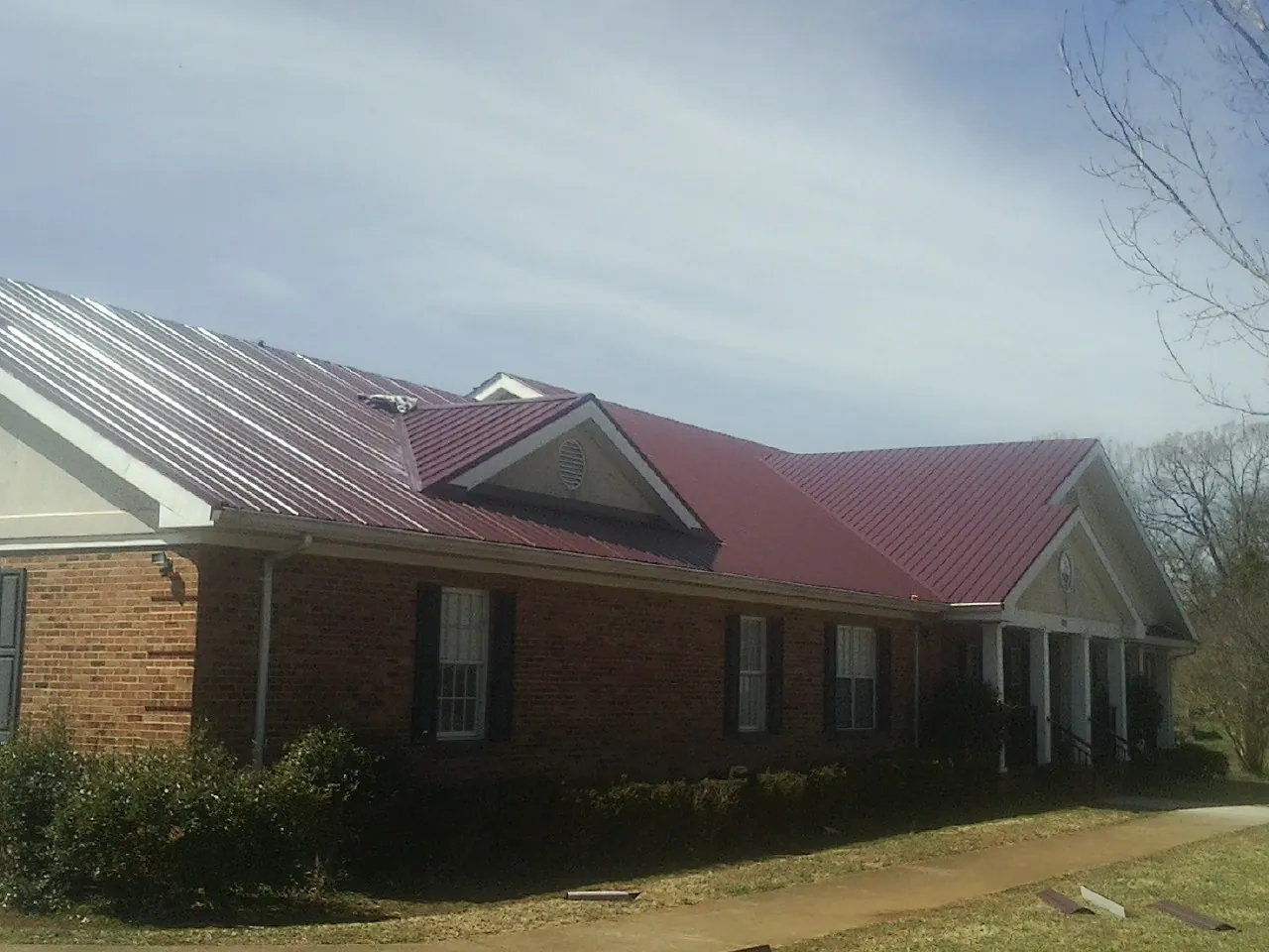 Red metal roof with gabled entries on a long brick building, from a Hail Damage Roof Repair job in Boardman