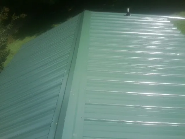 New green metal panels meeting at the ridge of a roof — Flat Roof Repair work by our crew in Boardman