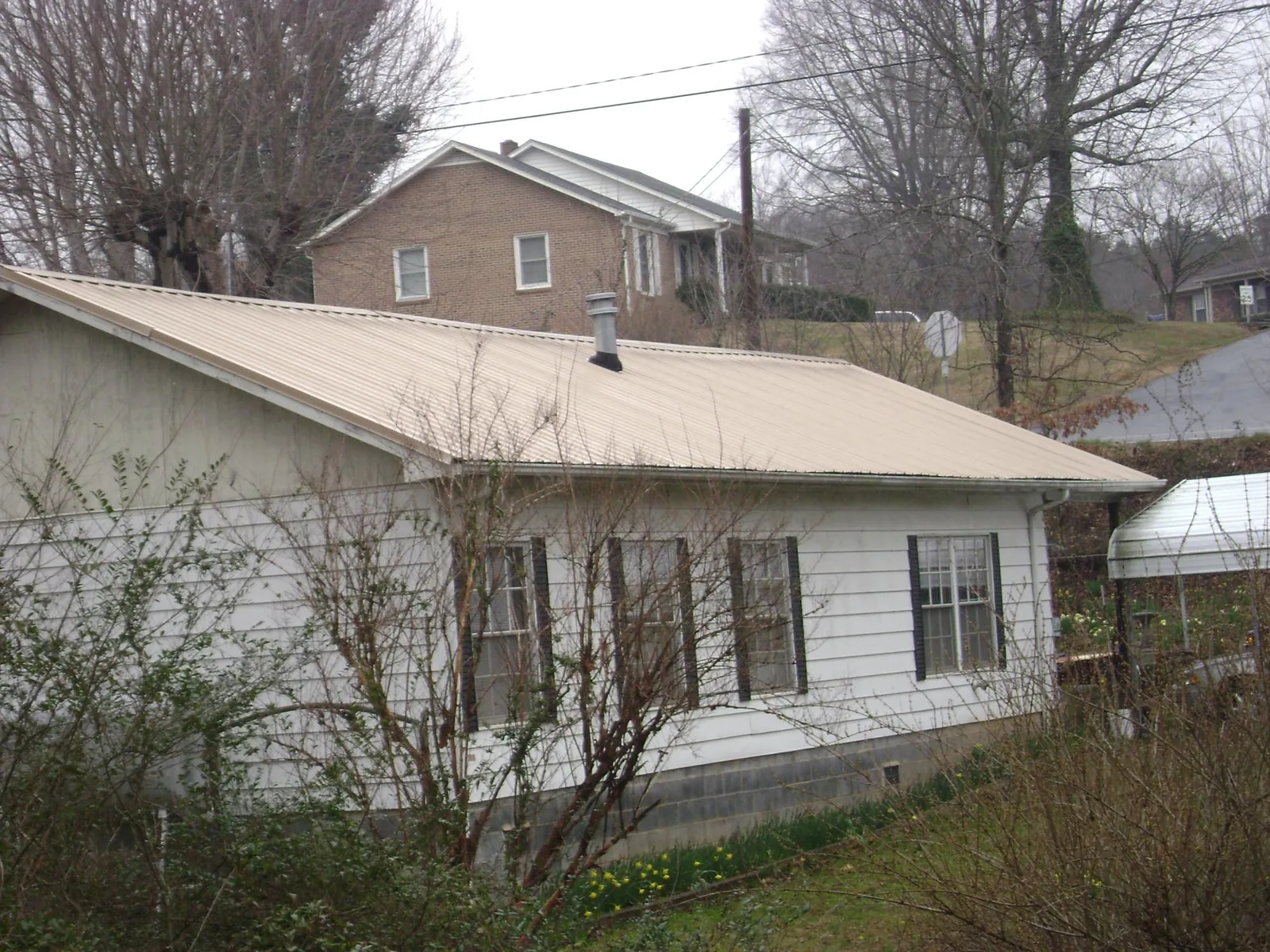 Tan metal roof on a white sided house set into a hillside — Commercial Roofing by Roofing Brothers in Boardman